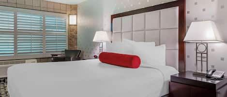 A hotel room with a large bed, two bedside lamps, a telephone, and a desk with a chair.