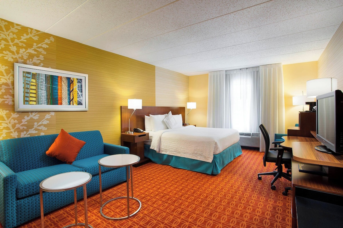 A hotel room with a bed, a sofa, a desk, and a TV.