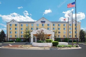 Un hotel Fairfield Inn & Suites by Marriott con una entrada central, asta de banderas y un área ajardinada al frente.