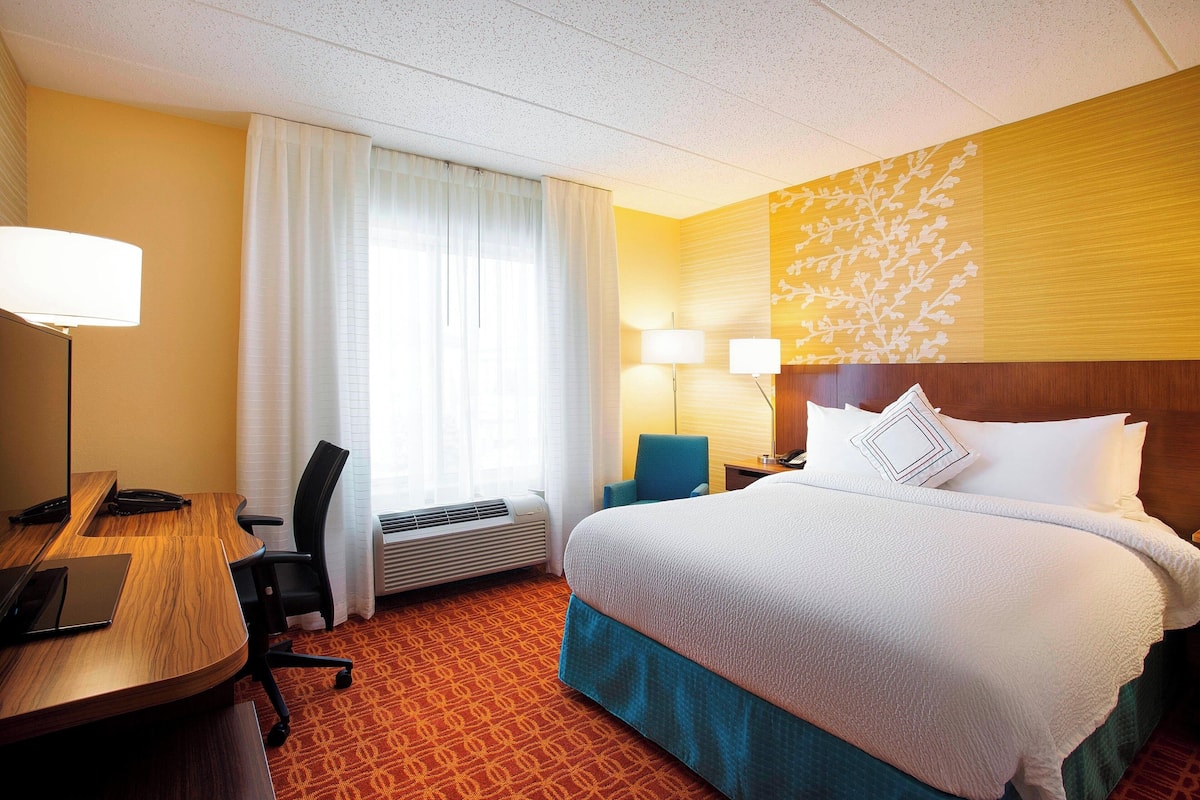 A hotel room with a bed, desk, chair, and two lamps.
