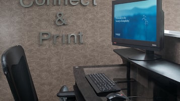 A computer desk with a monitor, keyboard, and mouse. The wall behind has a patterned design and the words "Connect & Print" are visible.