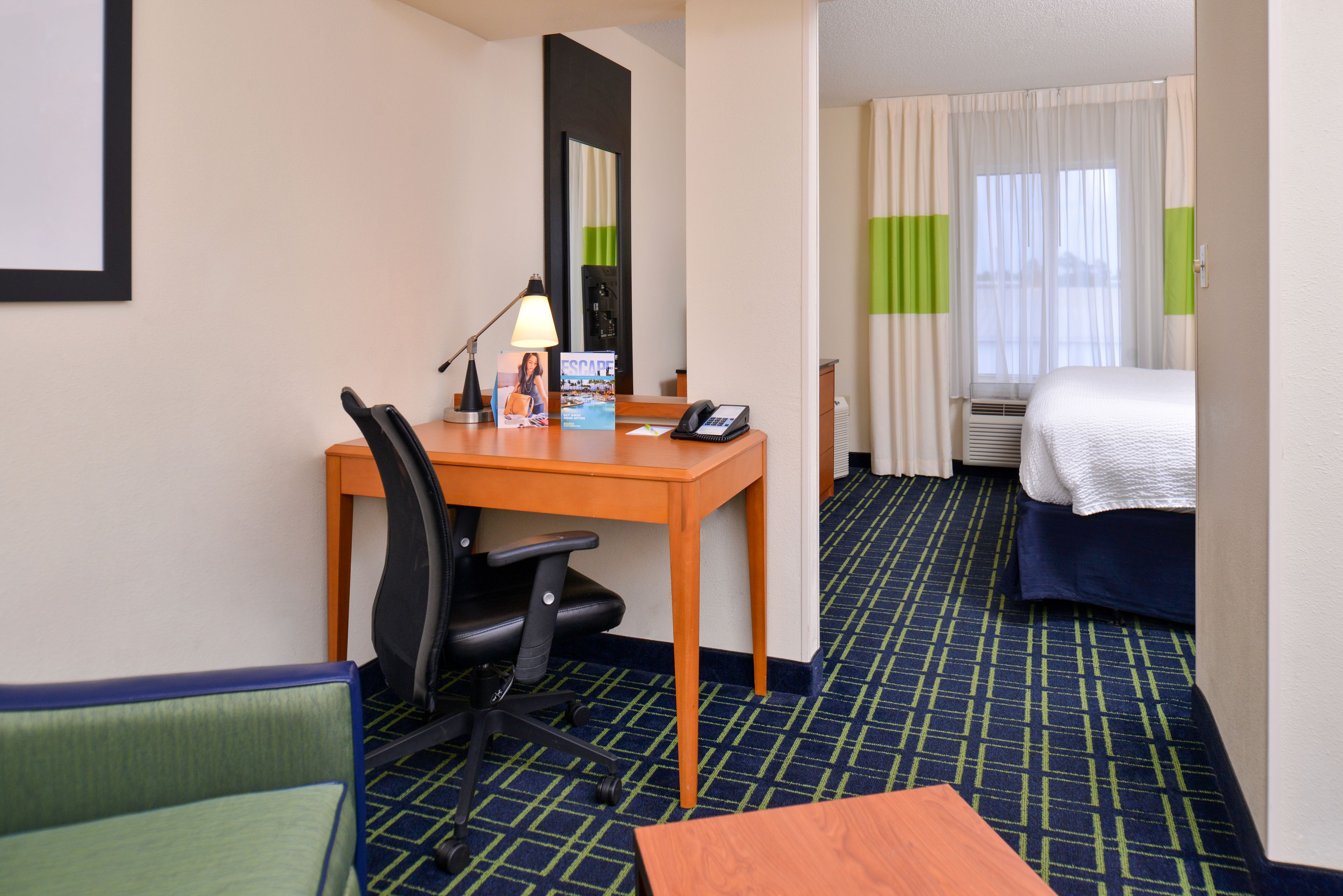 A hotel room with a desk, chair, bed, and a view of the outside through the window.