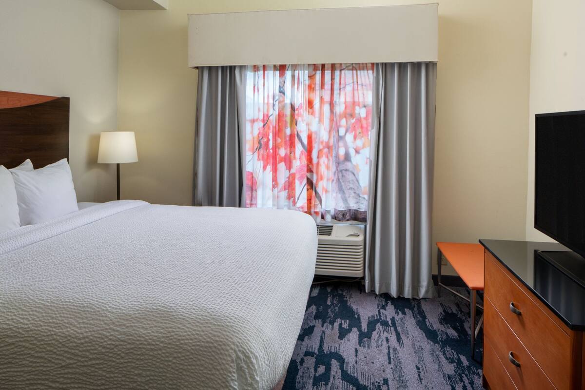 A hotel room with a large bed, a desk, a television, and a window with curtains.
