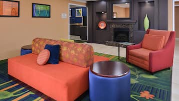 Habitación de hotel con sofá, sillón y reposapiés, una chimenea, y una cocina visible a través de una puerta abierta.