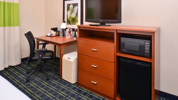 Habitación de hotel con escritorio, televisión, microondas, refrigerador pequeño y una silla.