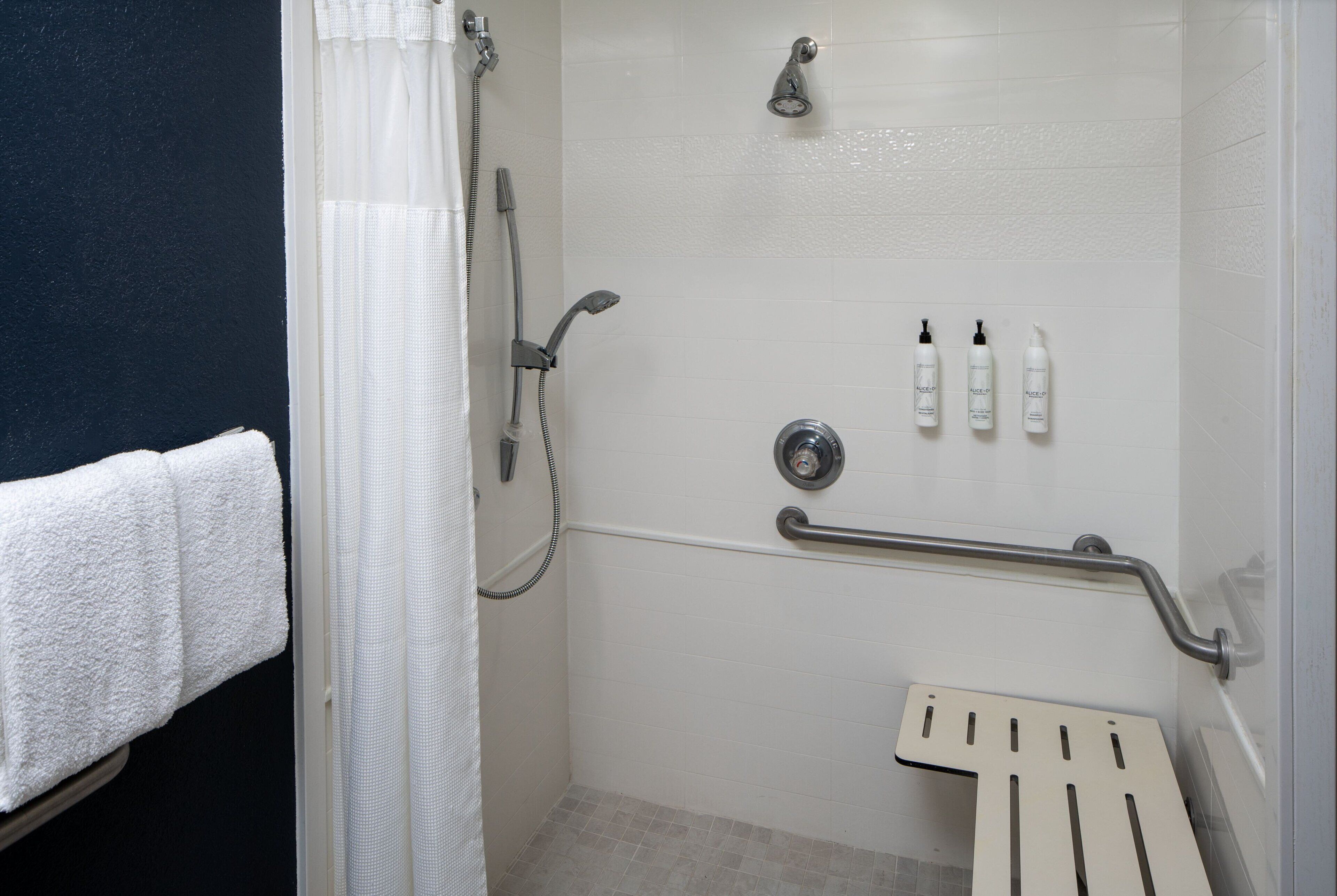 Un espace douche équipé d’une barre d’appui, d’un pommeau de douche à main et de trois bouteilles de shampoing.