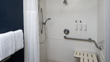 Un espace douche équipé d’une barre d’appui, d’un pommeau de douche à main et de trois bouteilles de shampoing.