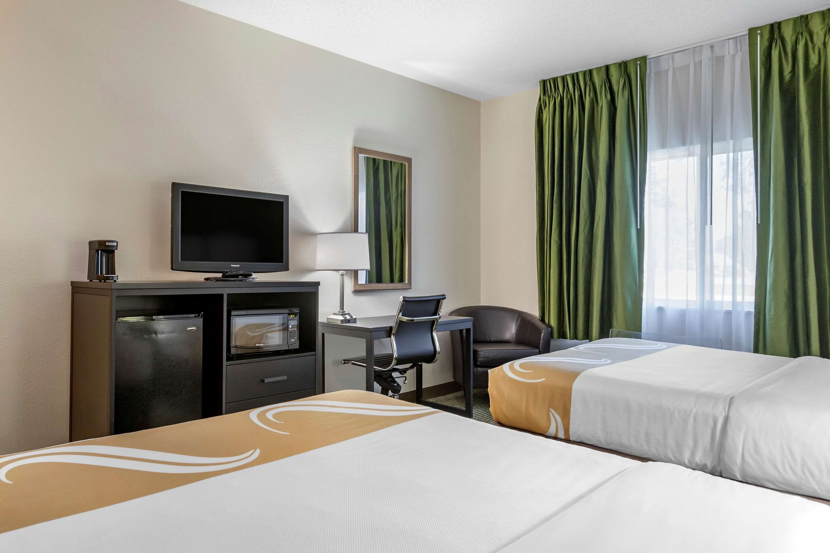 Una habitación de hotel con dos camas, un escritorio con computadora, televisión y un minibar.