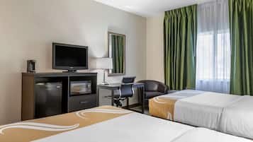 Una habitación de hotel con dos camas, un escritorio con computadora, televisión y un minibar.