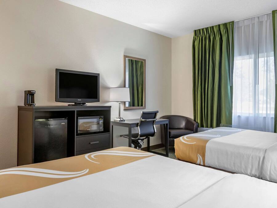 Una habitación de hotel con dos camas, un escritorio con computadora, televisión y un minibar.