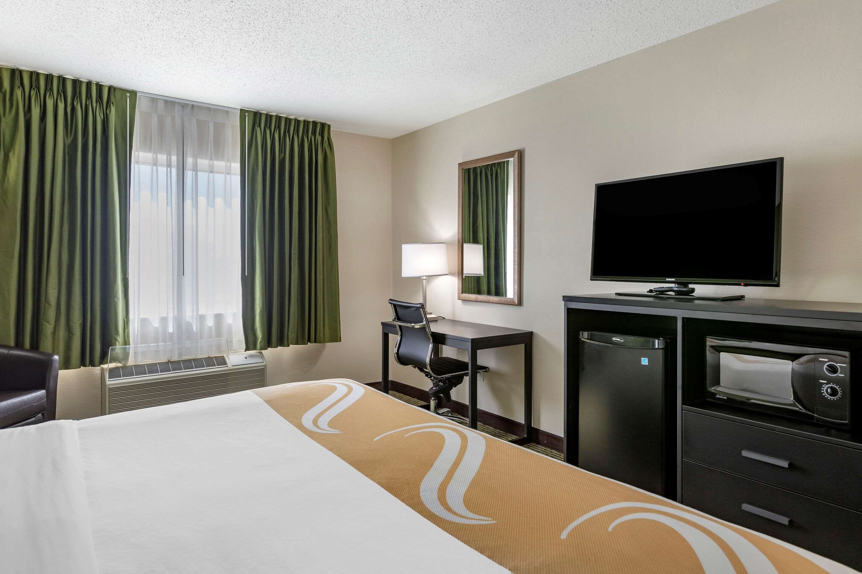A hotel room with a bed, a desk, a television, a mirror, and a window with curtains.