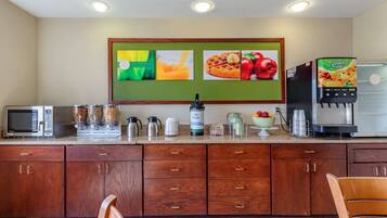 A kitchen with a microwave, toaster, coffee maker, and a fruit dispenser.