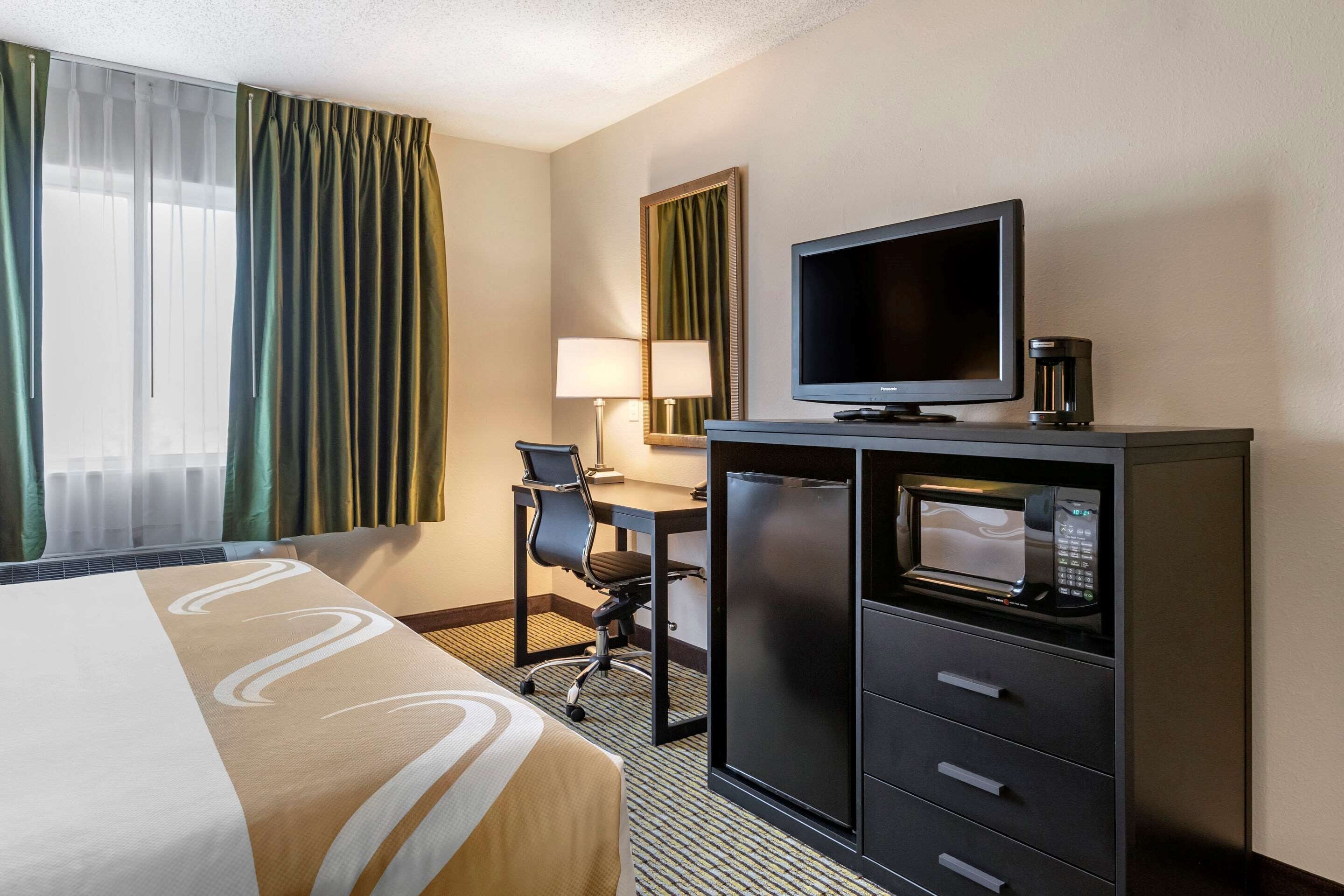 Une chambre d’hôtel équipée d’un lit, d’un bureau avec une chaise, d’une télévision, d’un four à micro-ondes et d’une lampe.