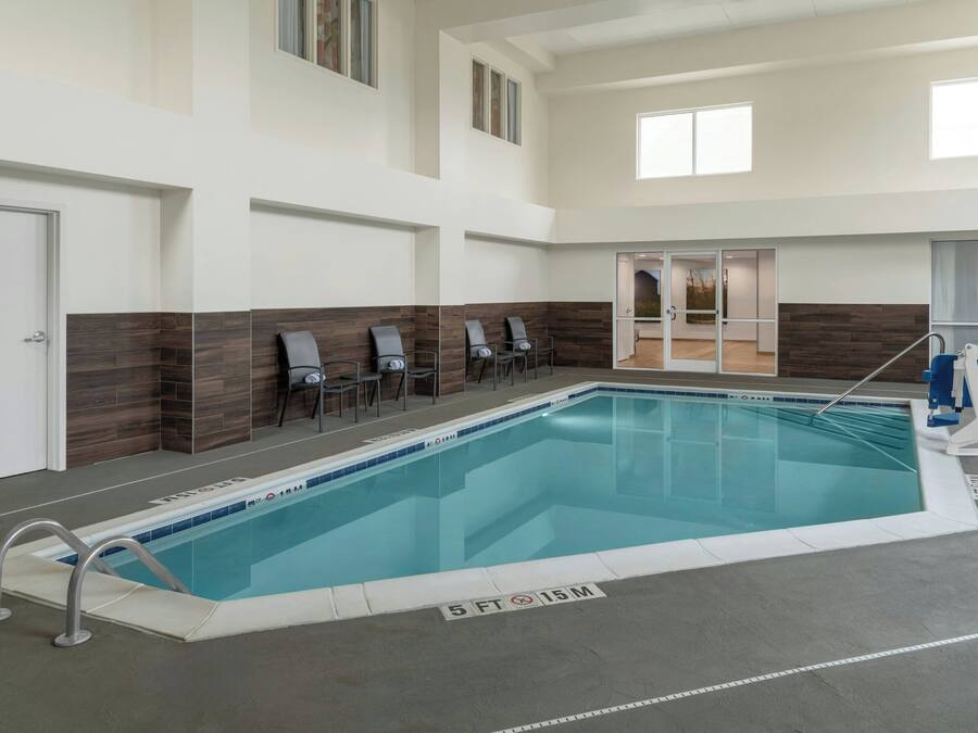 An indoor swimming pool with a 5 ft depth, adjacent lounge chairs, and a clear view of the pool area.