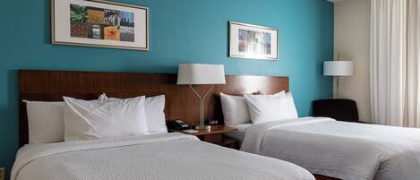 A hotel room with two beds, a wooden headboard, a nightstand with a lamp, and two framed pictures on the wall.