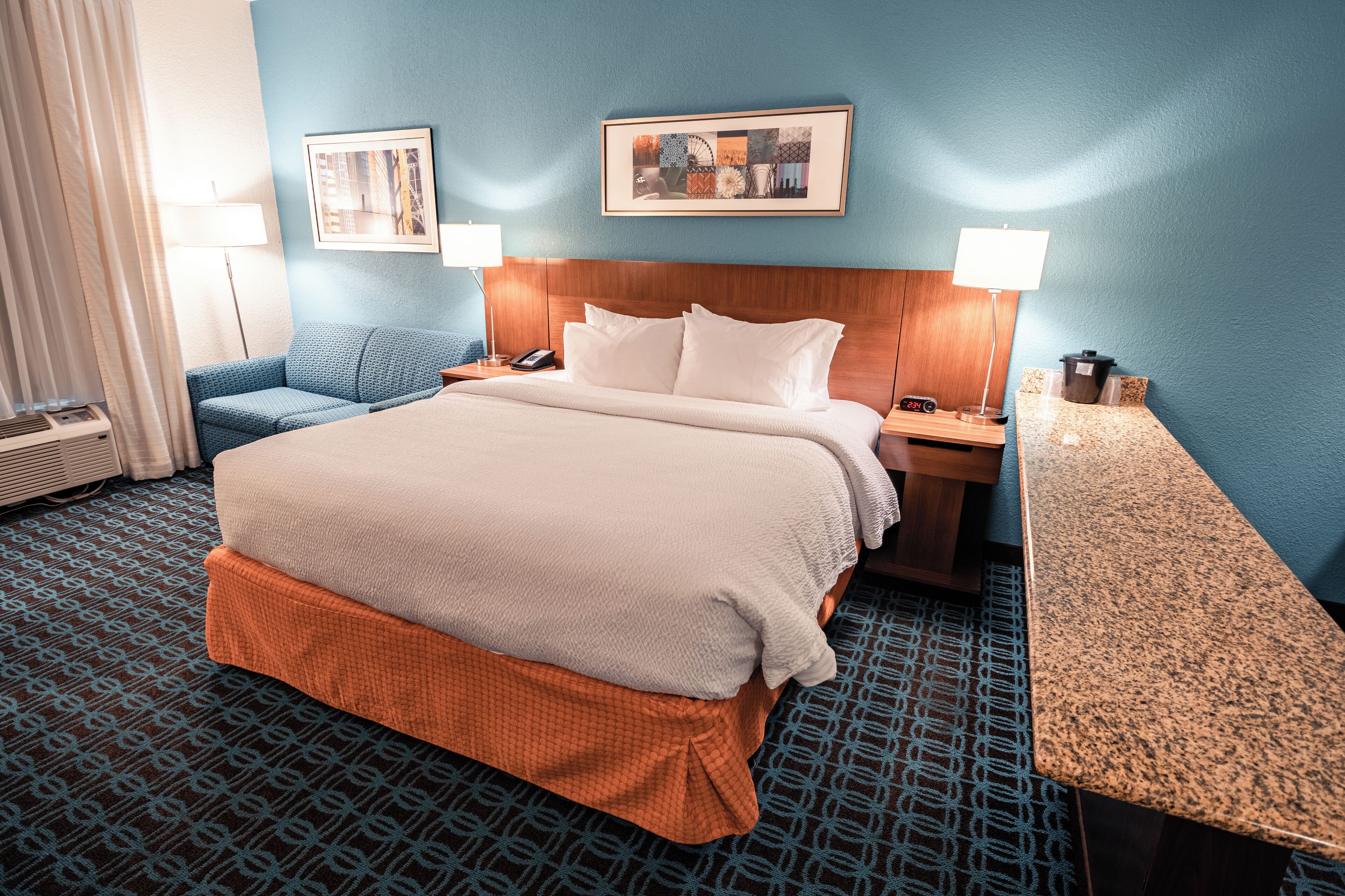 Ein Hotelzimmer mit einem großen Bett, einem blau gemusterten Teppich, zwei Wandlampen und einem gerahmten Bild über dem Bett.