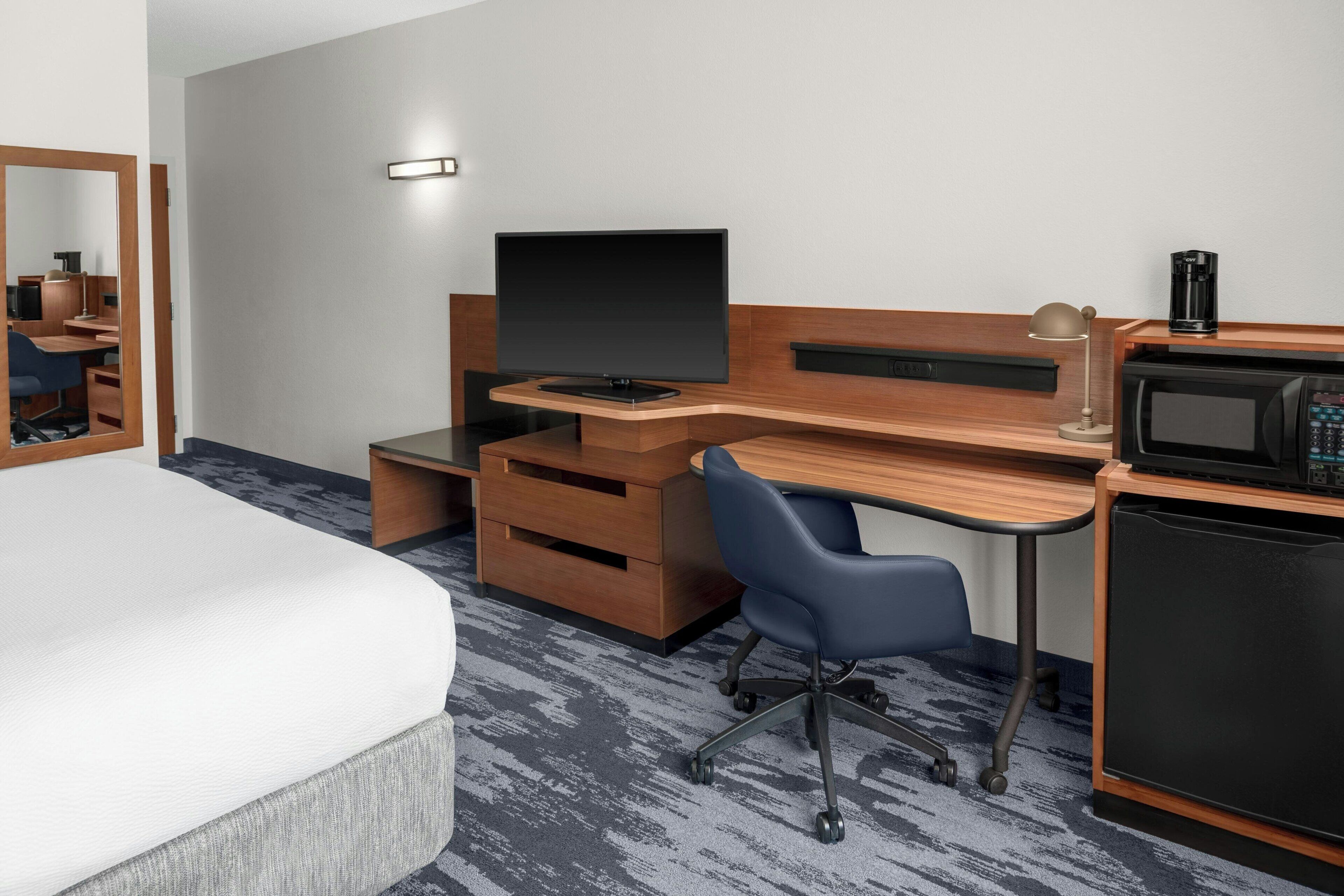 A hotel room with a bed, a desk with a computer, a chair, a microwave, and a coffee maker.