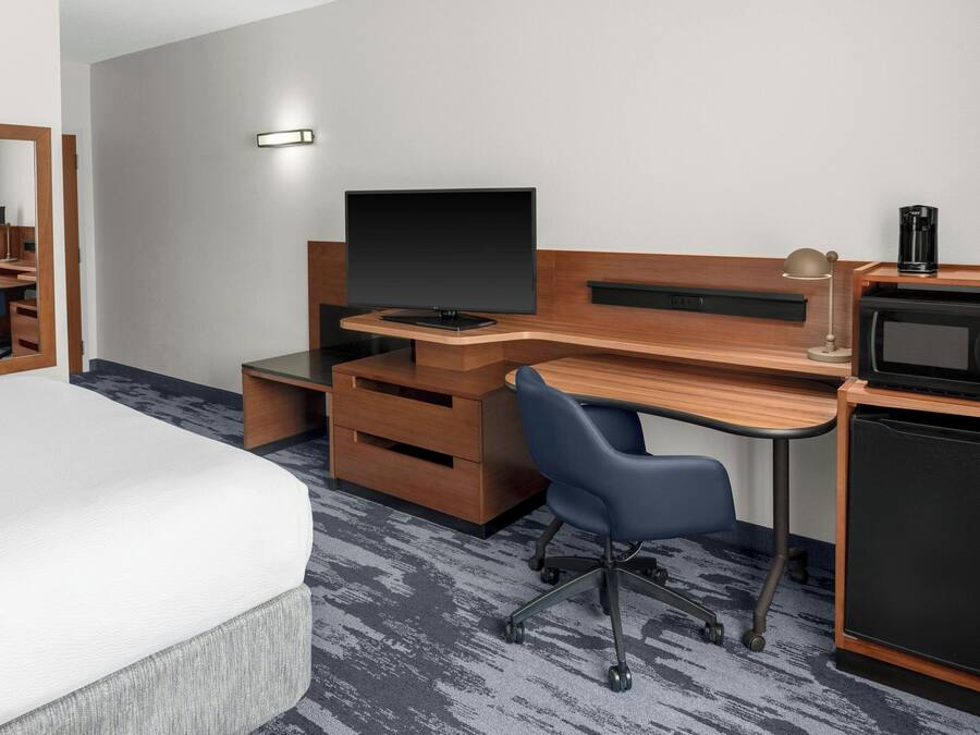 A hotel room with a bed, a desk with a computer, a chair, a microwave, and a coffee maker.