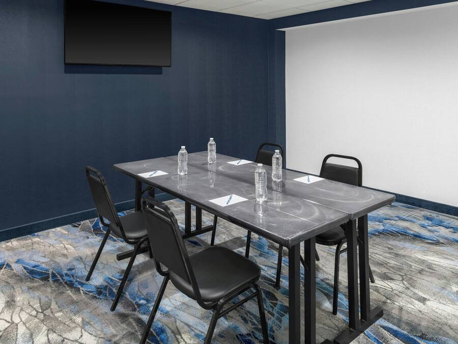 A conference room with a dark blue wall, a large projector screen, a marble table, and four black chairs.