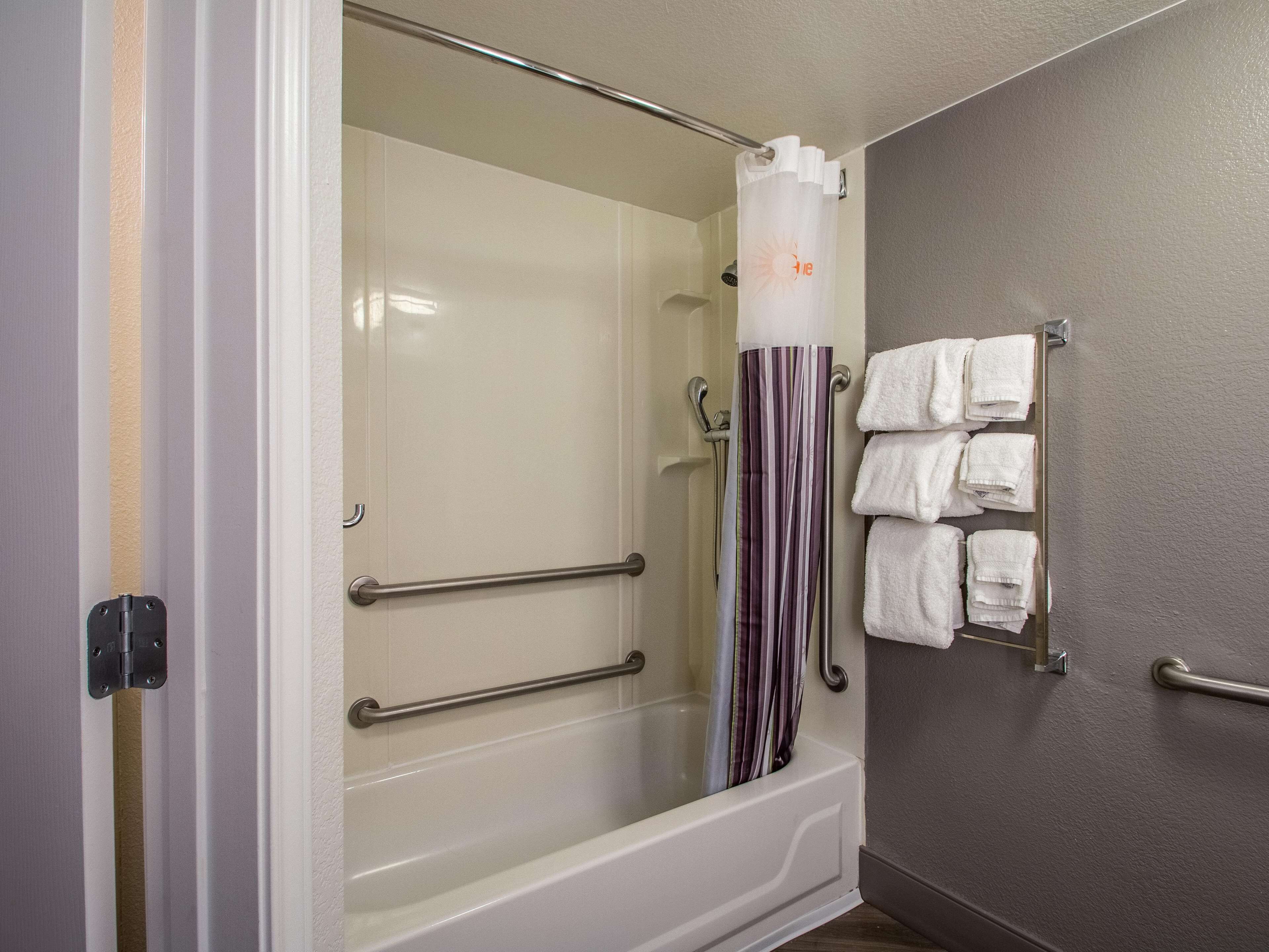 Ein Badezimmer mit einer gläsernen Duschkabine, einer weißen Badewanne, einem gestreiften Duschvorhang und einem Handtuchhalter mit mehreren weißen Handtüchern.