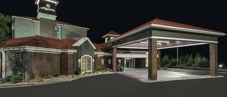 A hotel with a prominent sign, a covered entrance, and a well-lit driveway.