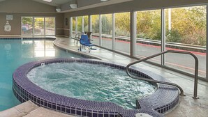 An indoor swimming pool with a hot tub, large windows, and a view of the outside.