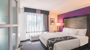 A hotel room with a large bed, a window with curtains, a framed picture on the wall, and a bedside lamp.