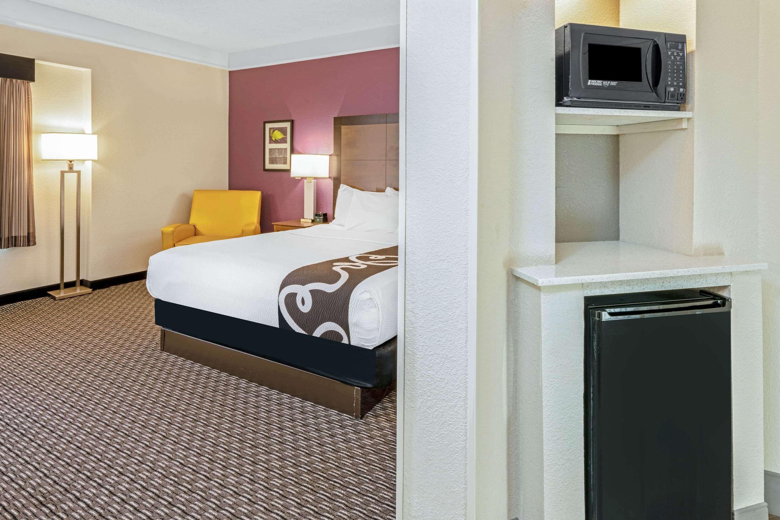 Camera d'albergo con un letto, una sedia, una scrivania con una lampada, un forno a microonde e un frigorifero.