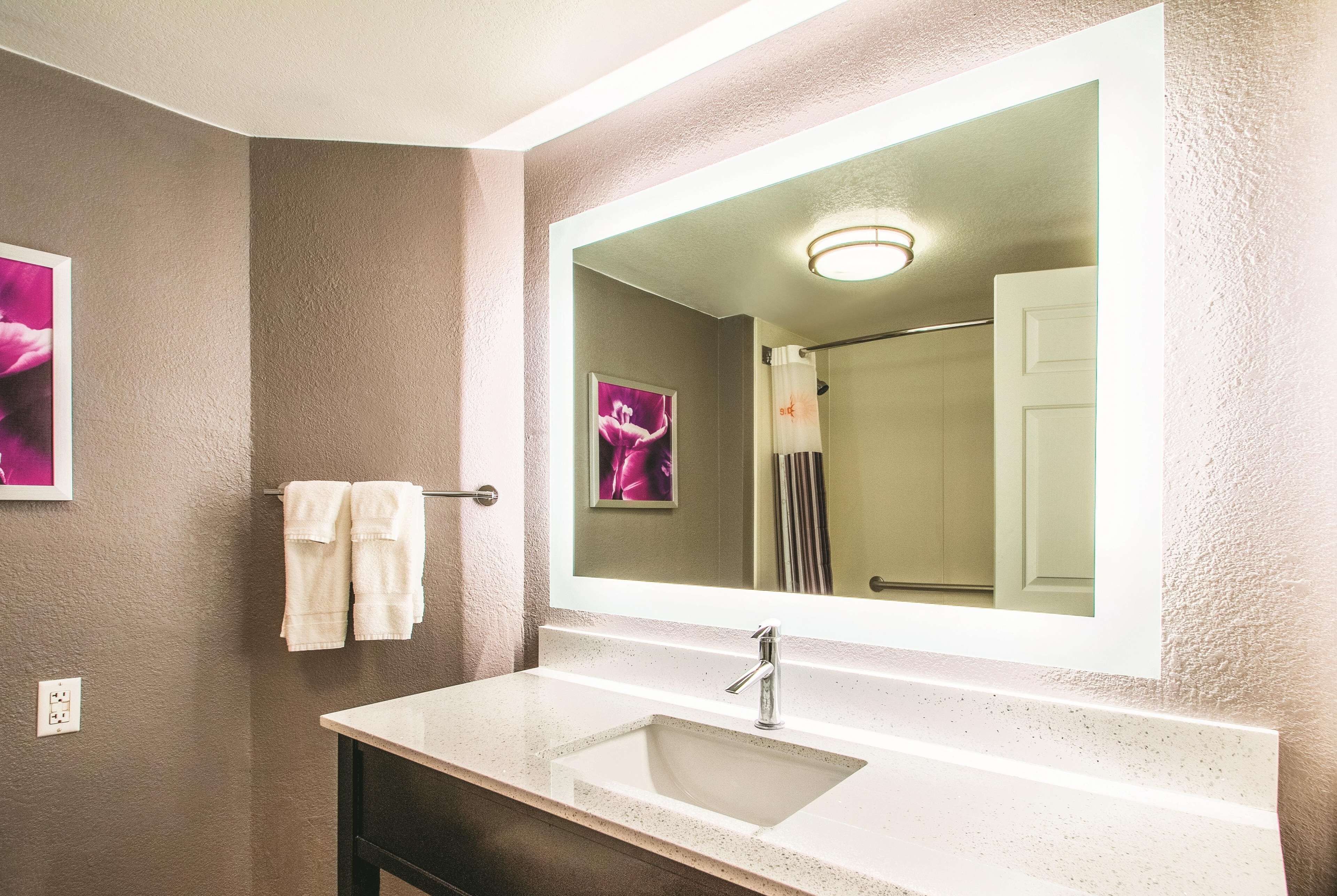 A bathroom with a large mirror, a sink, and a towel rack.