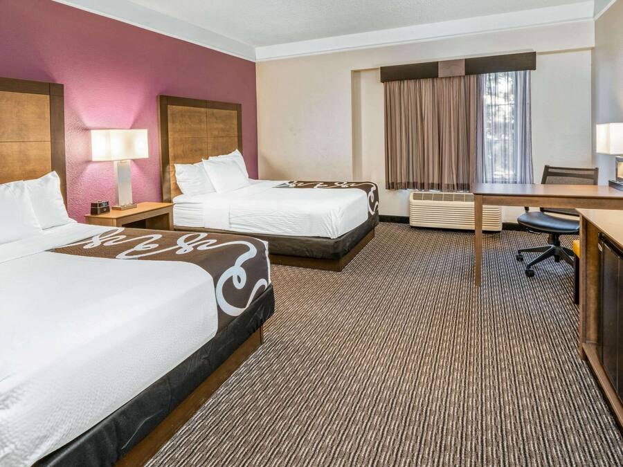 Habitación de hotel con dos camas, un escritorio, una silla, un televisor y una ventana con cortinas.