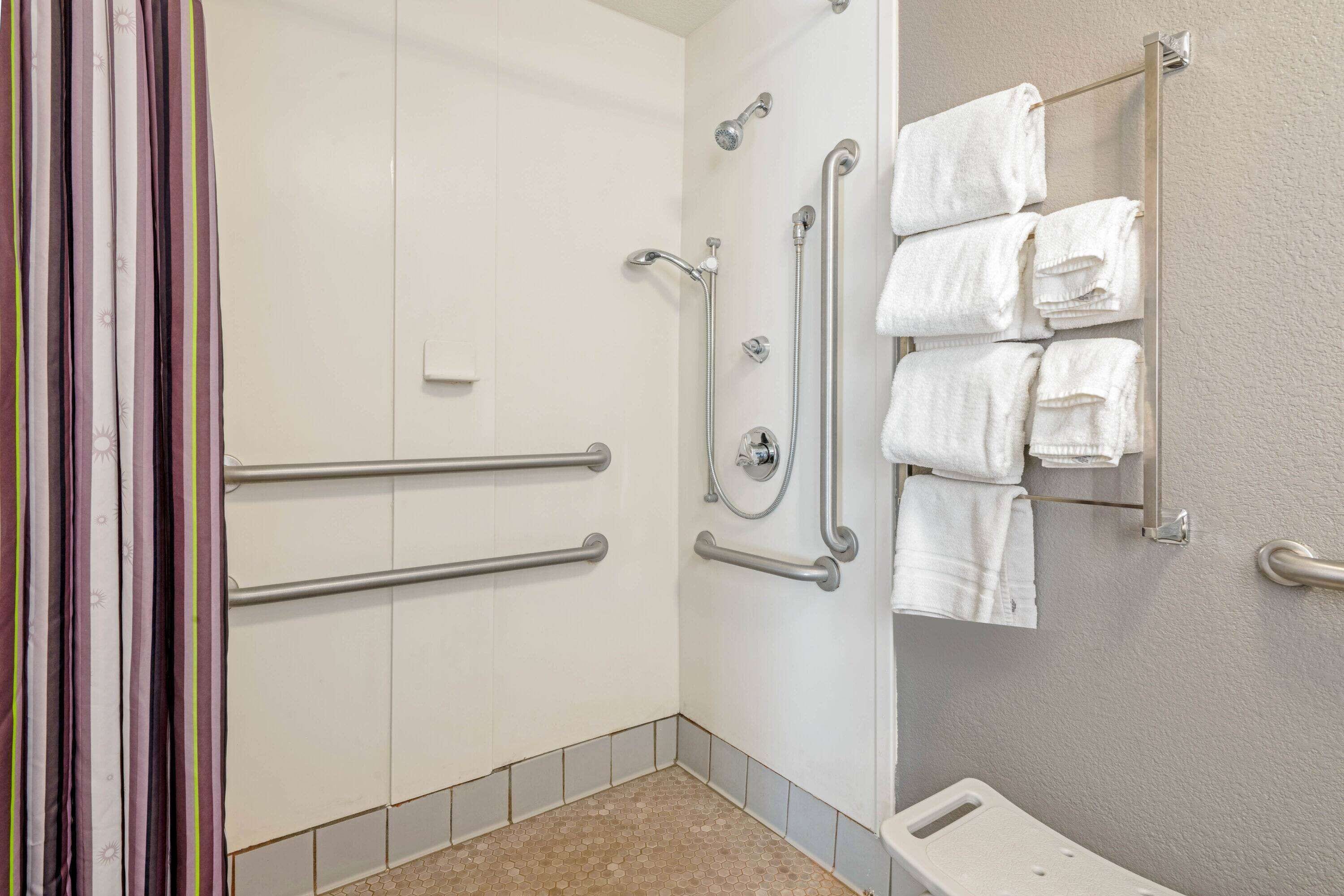 A bathroom with a shower, grab bars, a towel rack, and a toilet.
