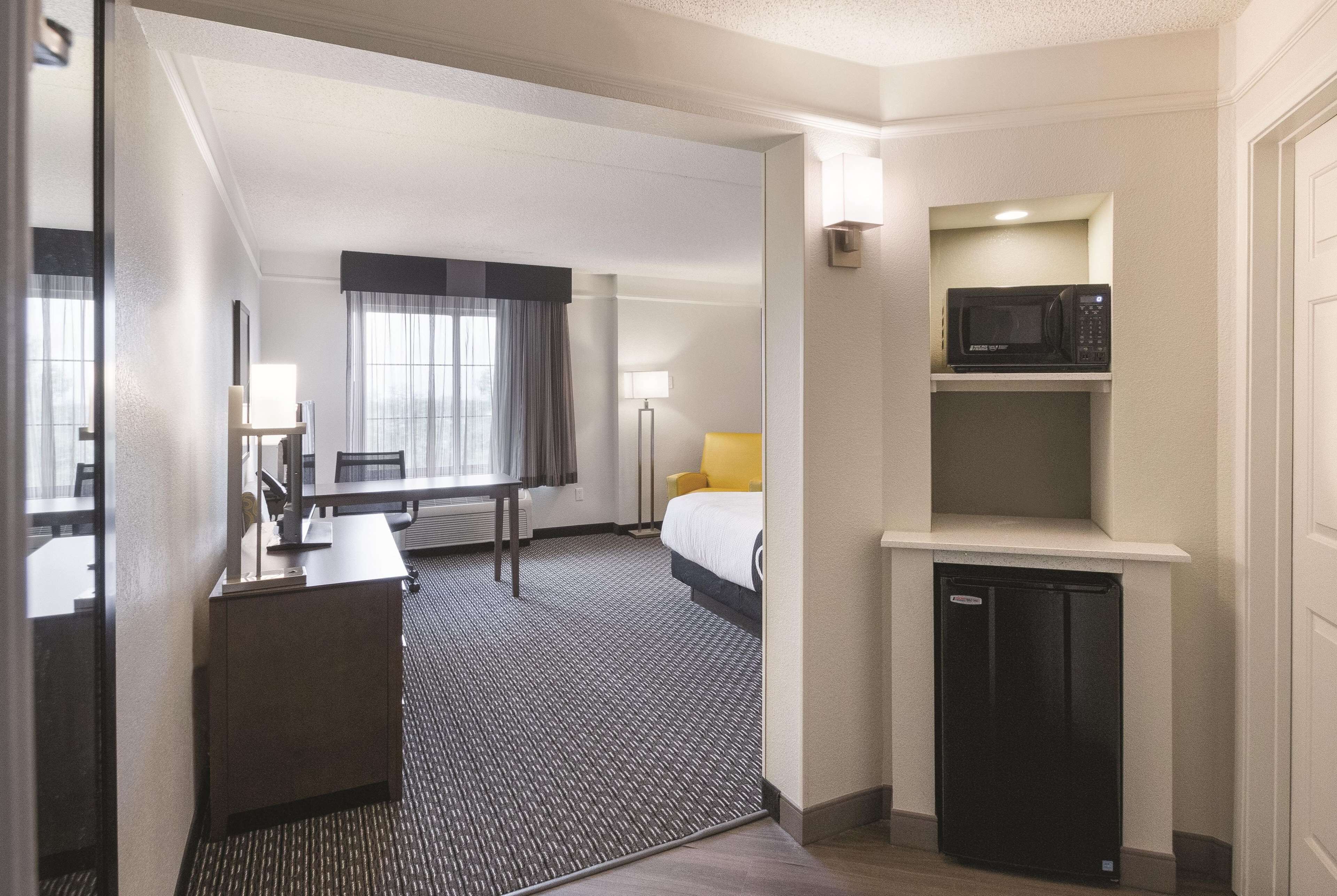 A hotel room with a desk, bed, bedside lamp, and a microwave on a shelf.