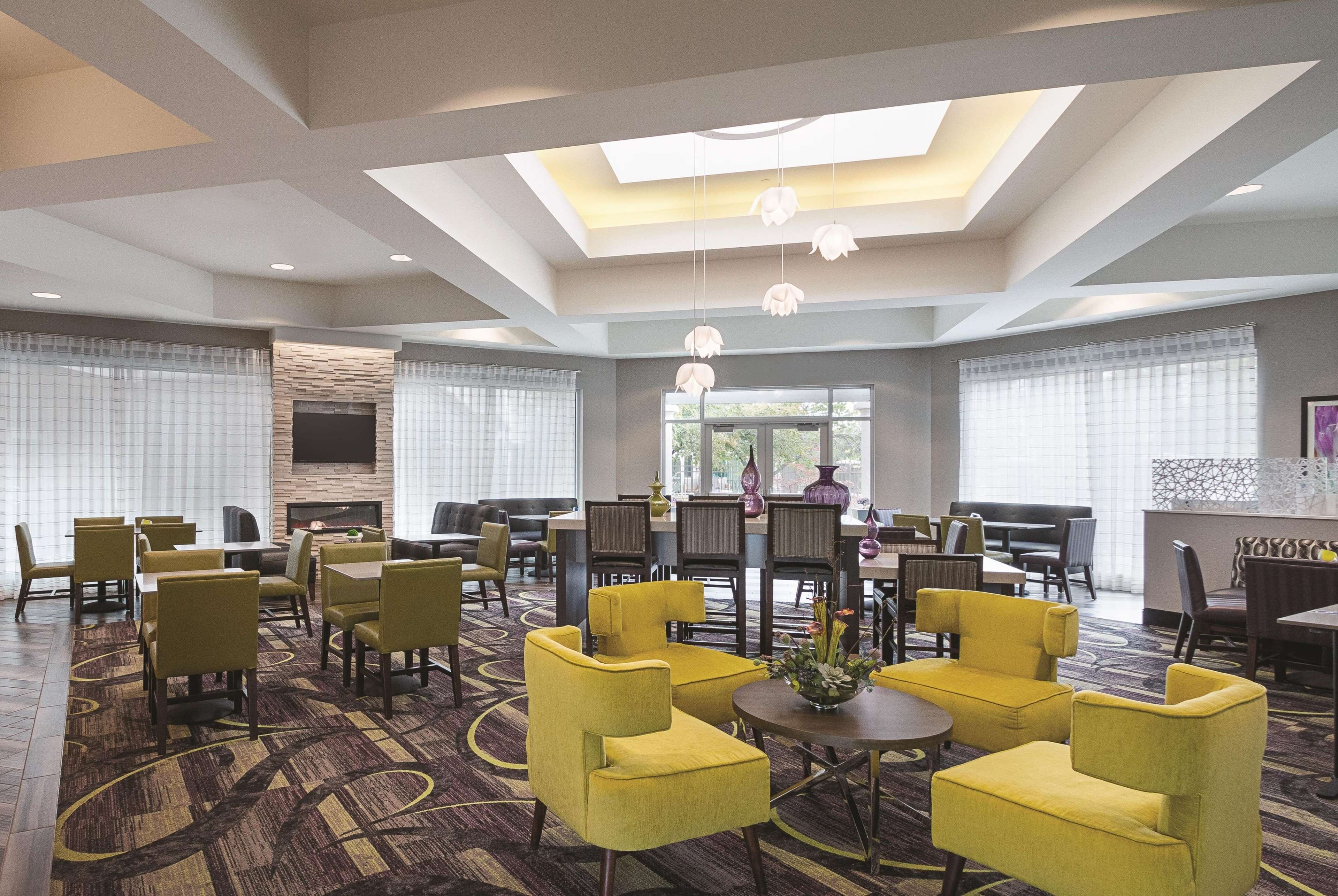 A spacious hotel lobby with yellow armchairs, a fireplace, and a large window providing natural light.