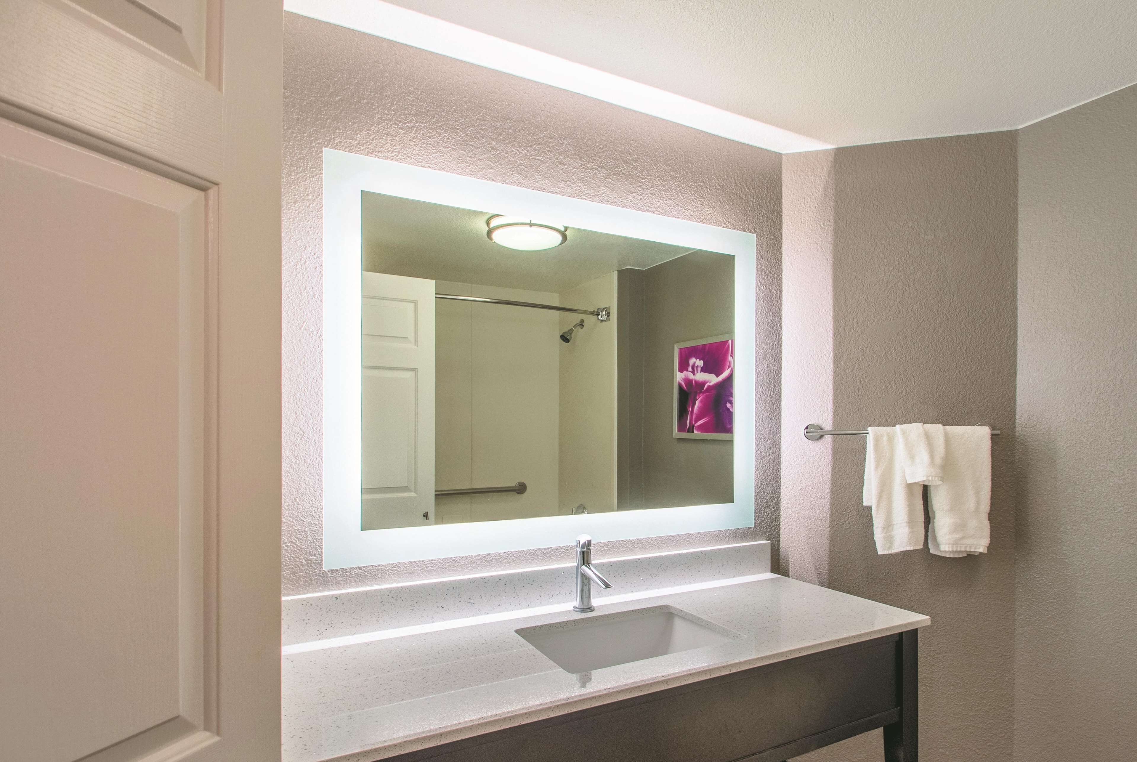 A bathroom with a large mirror, a sink, and a towel rack.