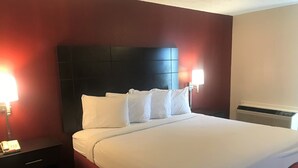 Una habitación de hotel con una cama grande, cabecera oscura, dos lámparas de noche y un calentador.