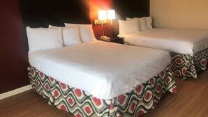 Habitación de hotel con dos camas, una mesita de noche y una lámpara de pared.