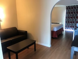 Una habitación con sofá, una mesita, una cama con colcha roja y una cortina estampada.