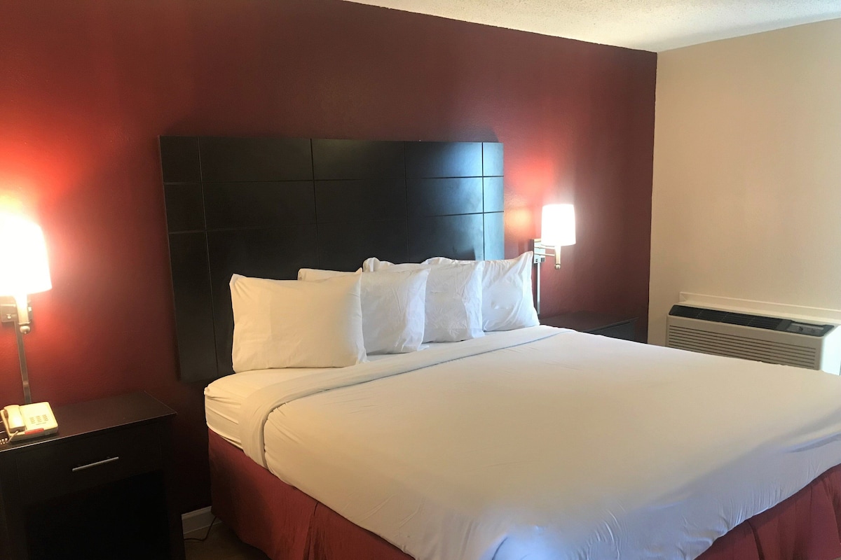A hotel room with a large bed, a nightstand, a lamp, and a wall-mounted heater.