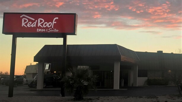 Un letrero de Red Roof Inn & Suites con un edificio moderno al fondo.