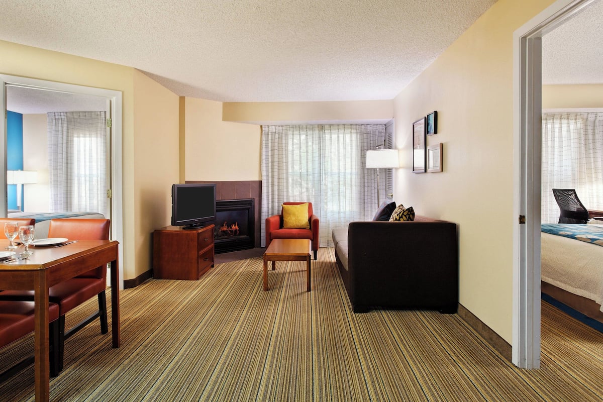 A hotel room with a dining table, a sofa, a TV, a fireplace, and a bed.