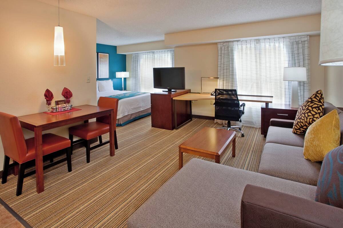A hotel room with a bed, a desk with a chair, a sofa, a TV, and a lamp.