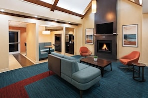 A modern lounge area with a sofa, armchairs, a coffee table, a fireplace, and a television mounted on the wall. - Residence Inn Houston Sugar Land/Stafford (Stafford)