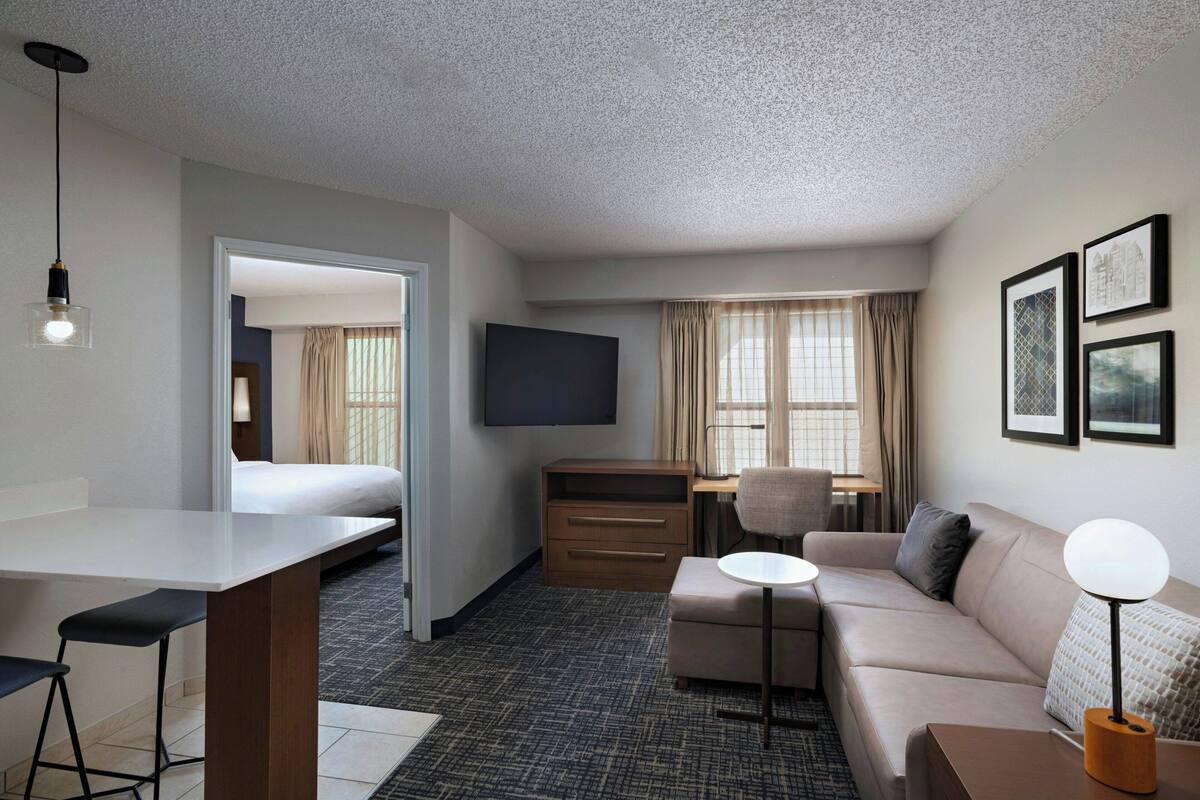 A hotel room with a bed, a desk, a sofa, a TV, and a dining area.