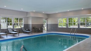 En indendørs swimmingpool med klart, blåt vand, omgivet af liggestole og et flisegulv.
