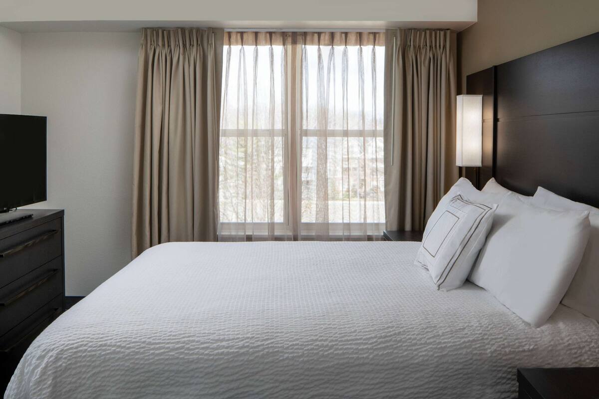 Una habitación de hotel con una cama grande, un televisor en una cómoda y una ventana con cortinas.