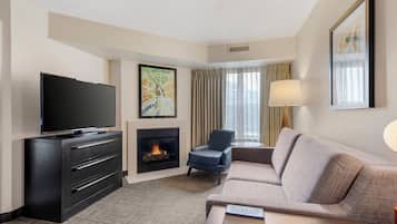 A hotel room with a flat-screen TV, a fireplace, a sofa, a chair, and a lamp.
