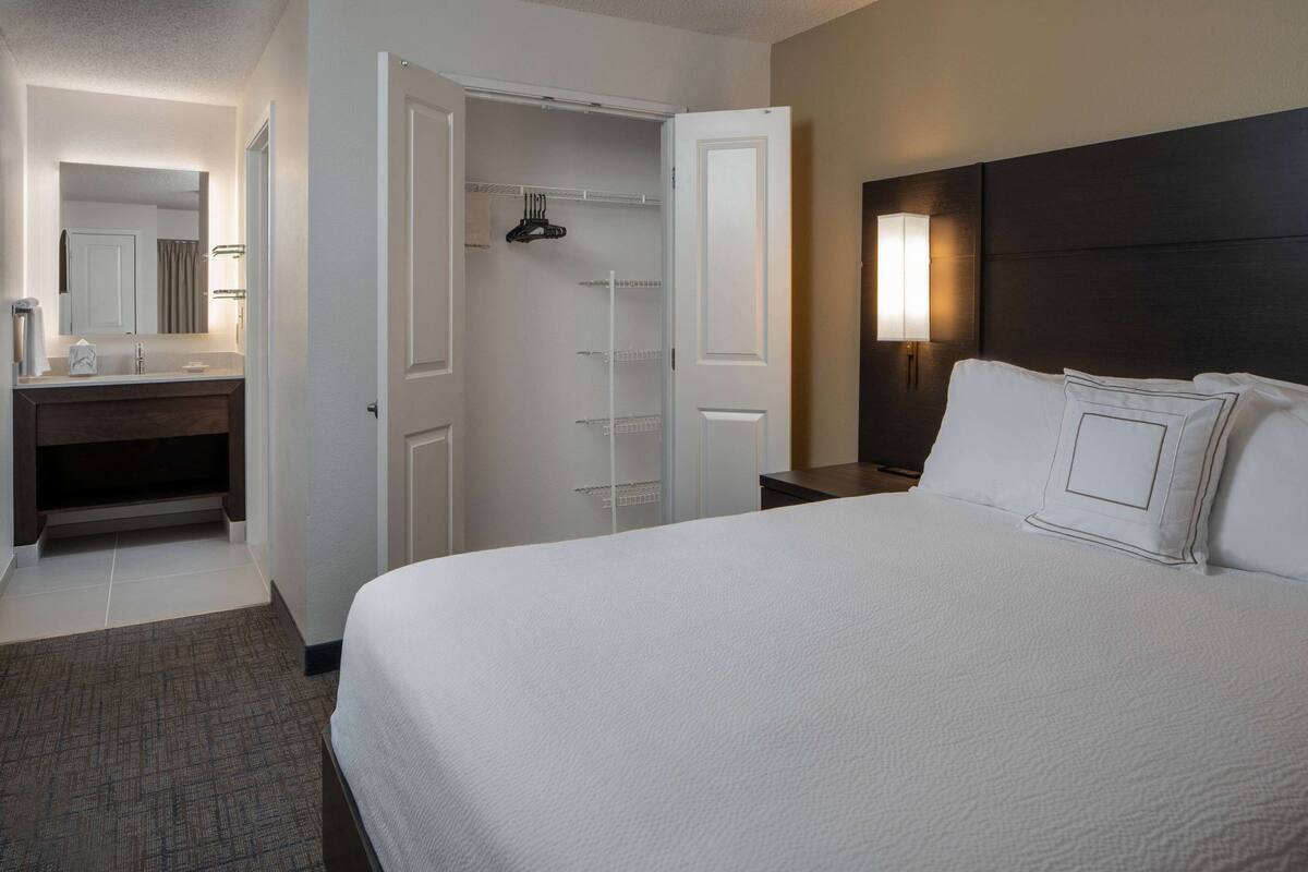 Una habitación de hotel con una cama grande, un baño con espejo, un armario y una mesita de noche.