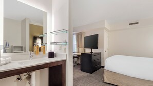A hotel room with a large mirror, two sinks, a desk, a flat-screen TV, and a bed. - Sonesta ES Suites Fairfax Fair Lakes (Fairfax)