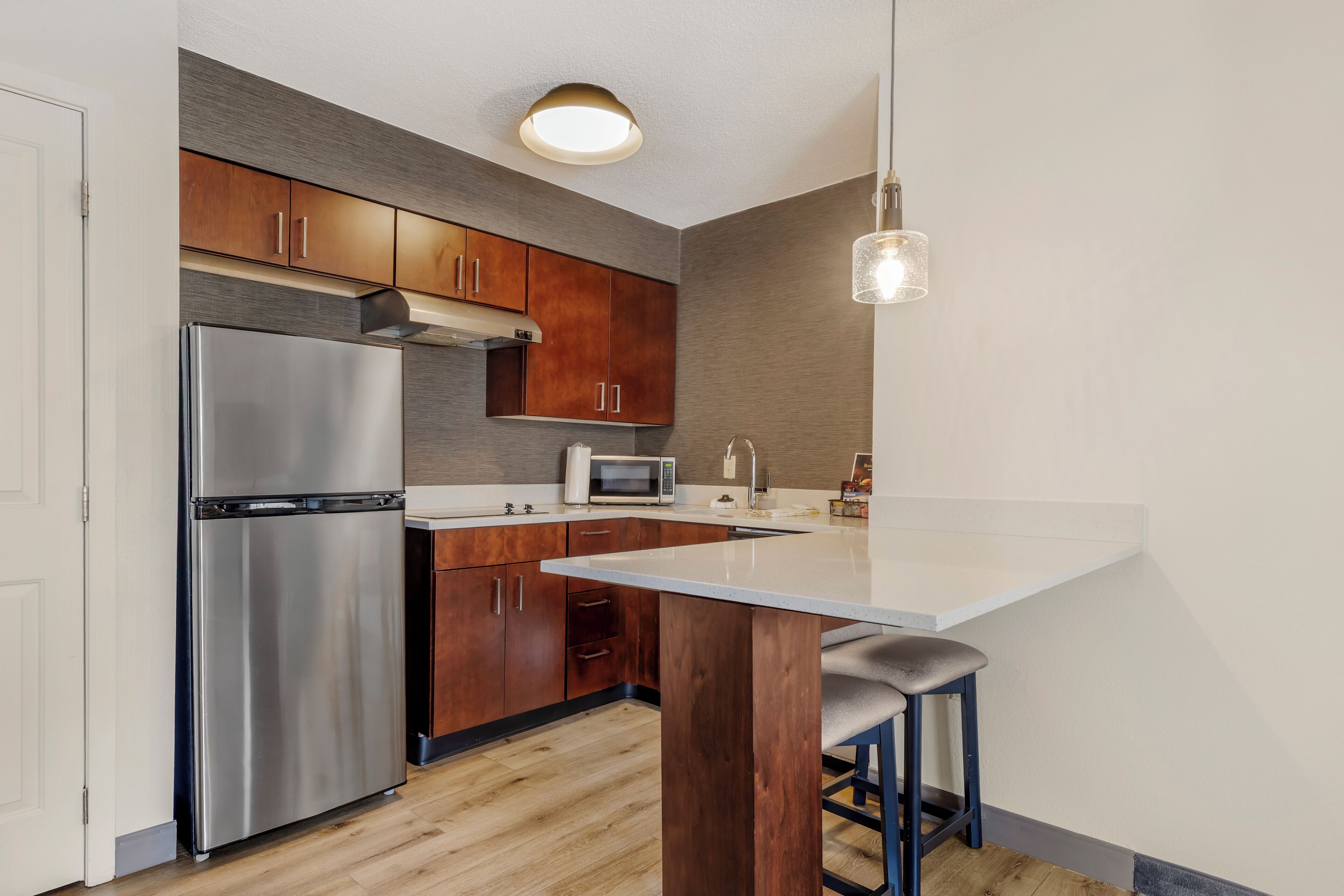 Een moderne keuken met houten kastjes, roestvrijstalen apparatuur en een centraal eiland met barkrukken.