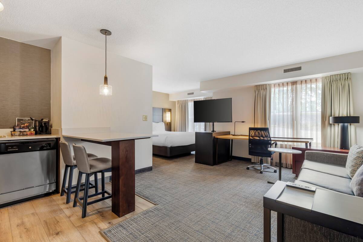 Una habitación de hotel con kitchenette, una cama, un escritorio, un sofá y un televisor.